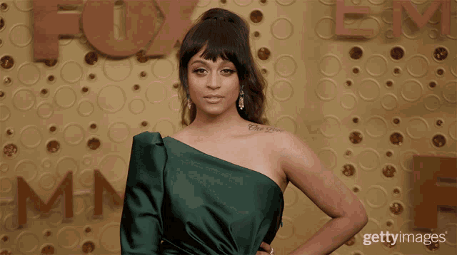 a woman in a green dress stands in front of a wall with the letters fox on it