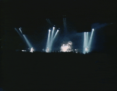 a blurred image of a band on stage with a crowd watching