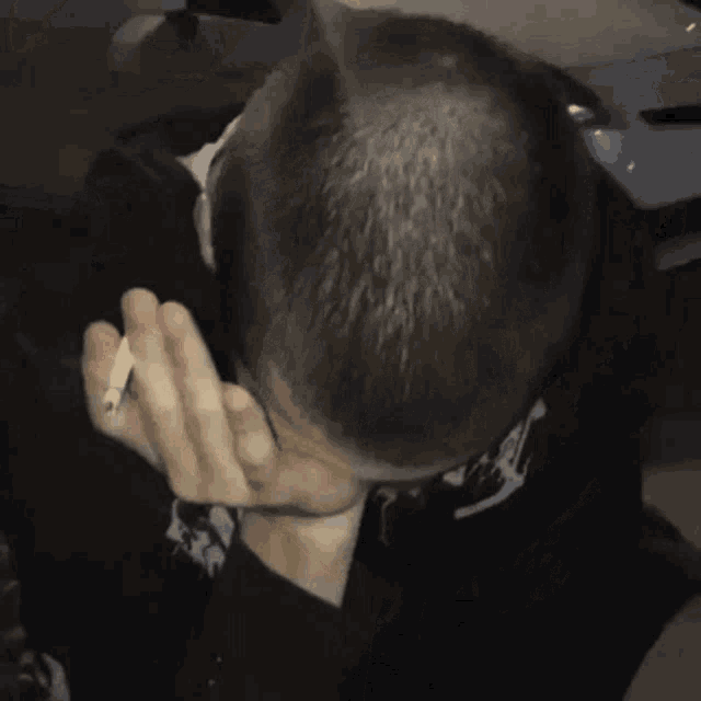 a man is covering his face with his hand while holding a cigarette