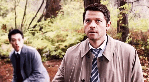 a man in a suit and tie is standing next to another man in a suit and tie in the woods .