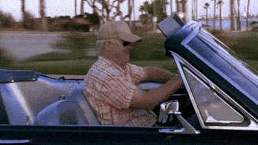 a man wearing sunglasses and a baseball cap is driving a car
