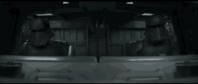 a man is sitting in the back of a vehicle with a few robots behind him