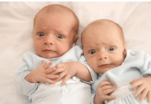 two newborn babies are laying next to each other on a bed and making funny faces .