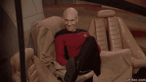 a bald man is sitting in a chair with his legs crossed .