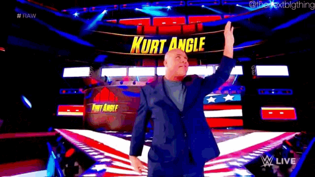 a man in a suit is standing on a stage in front of a sign that says kurt angle .