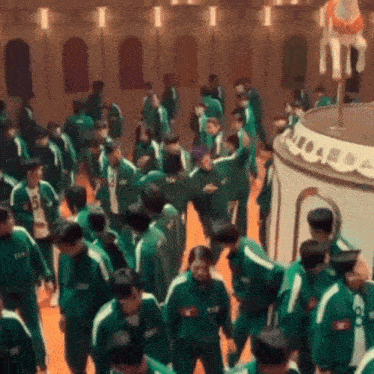 a large group of people are standing in a room wearing green uniforms .