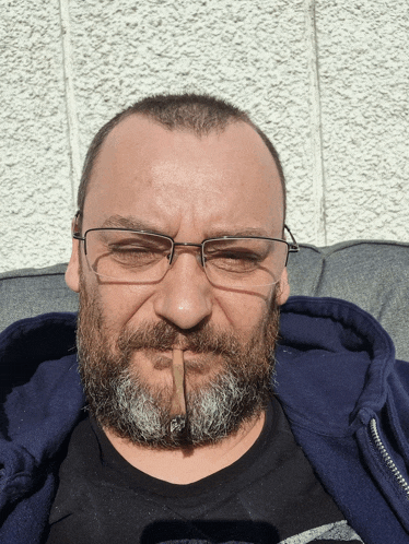 a man with glasses and a beard is holding a cigar in his mouth