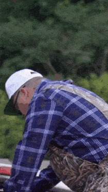 a man wearing a plaid shirt and a white hat with a fishing company logo on it