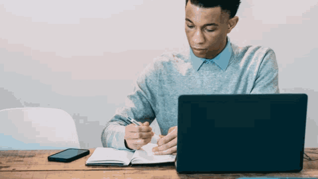 a man is writing in a notebook while using a laptop computer