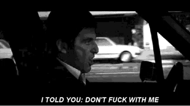 a man in a suit and tie is driving a car and yelling at another man .