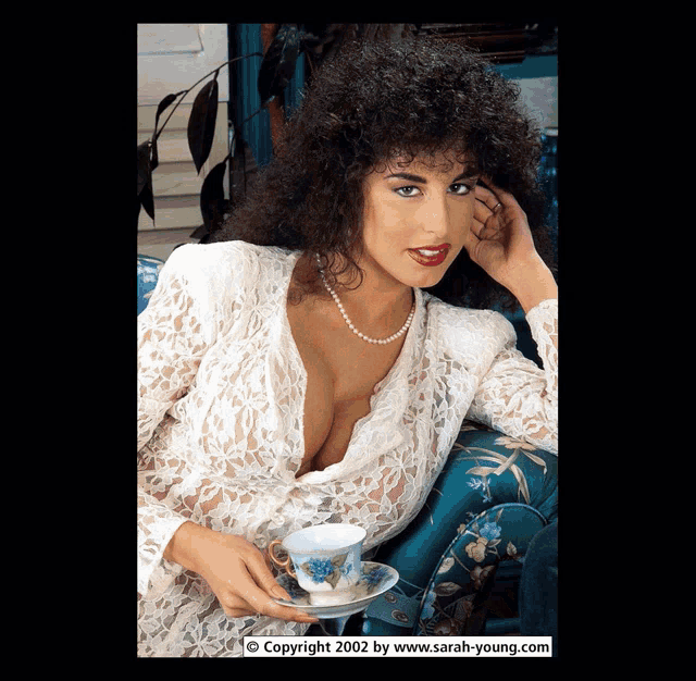 a woman sitting on a couch holding a cup and saucer with the copyright 2002 by www.sarah-young.com at the bottom