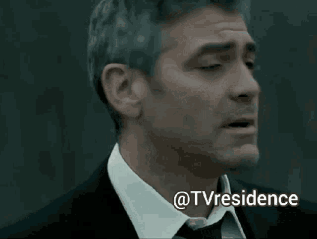 a man in a suit and tie is looking up with the words @tvresidence behind him