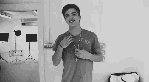 a black and white photo of a young man in a t-shirt standing in a room .
