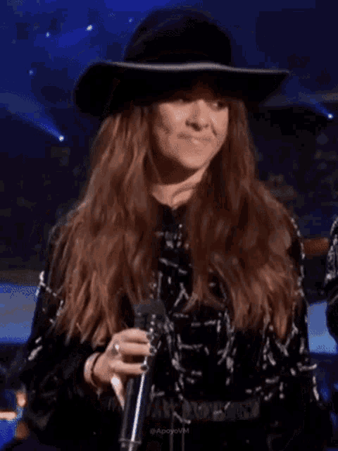 a woman wearing a hat and a black jacket is smiling while holding a microphone .