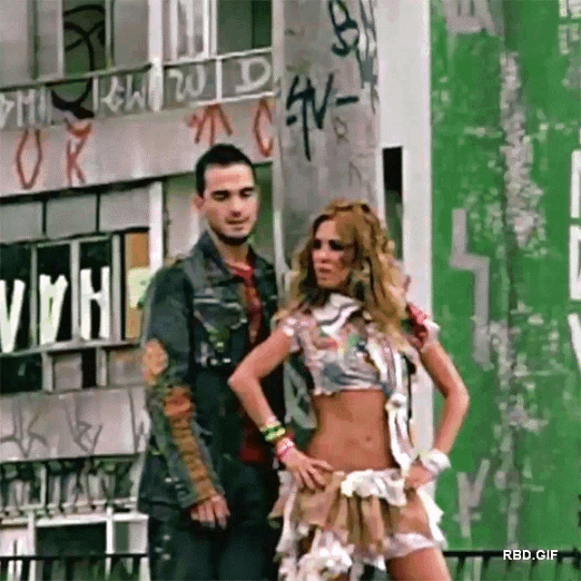 a man and a woman are standing in front of a building with graffiti on it that says ' rbd.gif '