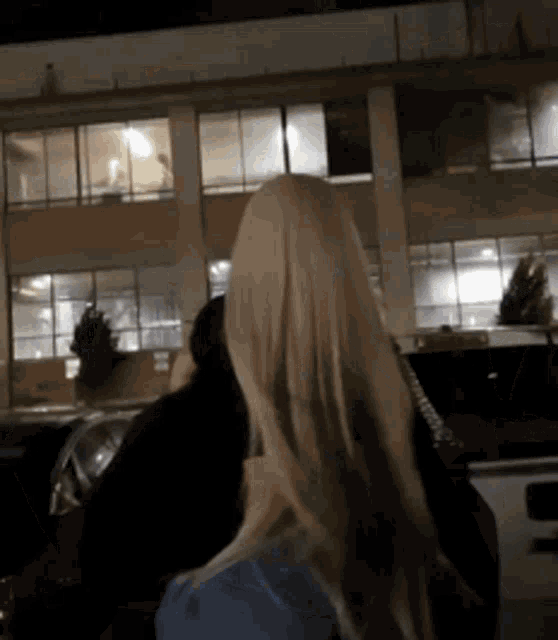 a woman with long blonde hair stands in front of a building