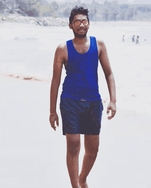 a young man wearing sunglasses and a blue tank top stands on a beach