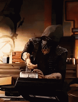 a man wearing a mask and a hooded jacket is sitting at a desk