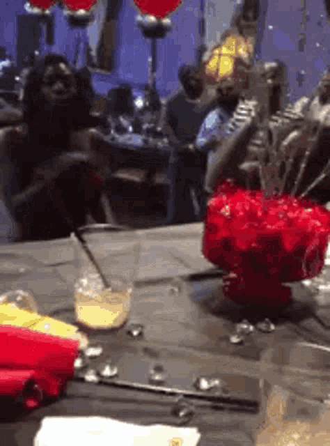a group of people are sitting at a table with a bowl of red flowers on it .