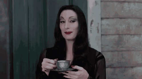 a woman in a black dress is holding a cup of coffee in her hands .