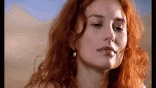 a woman with red hair is wearing earrings and looking at the camera .