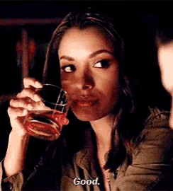 a woman is drinking a glass of whiskey and says good .