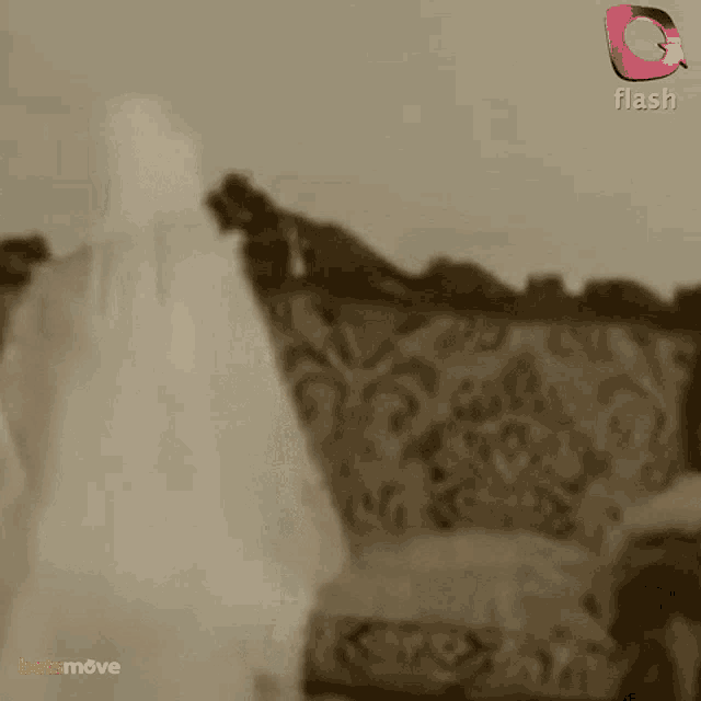 a woman in a white dress is standing in front of a couch with a flash logo in the background