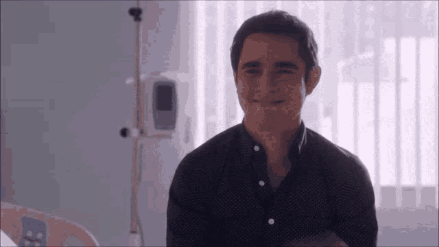 a man in a black shirt is smiling in a hospital bed