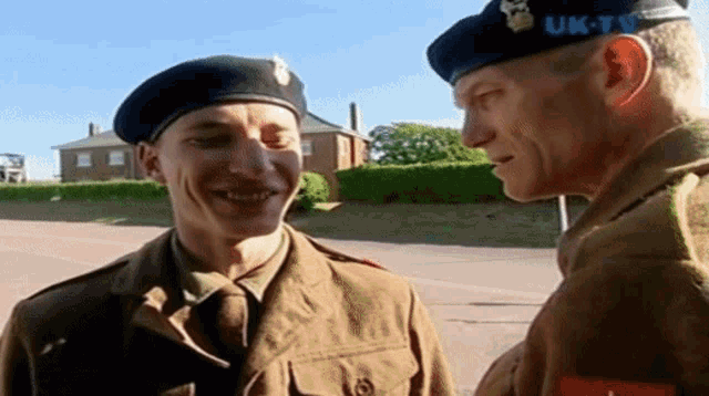 a man in a beret talks to another man in a military uniform with uk-tv written on his hat
