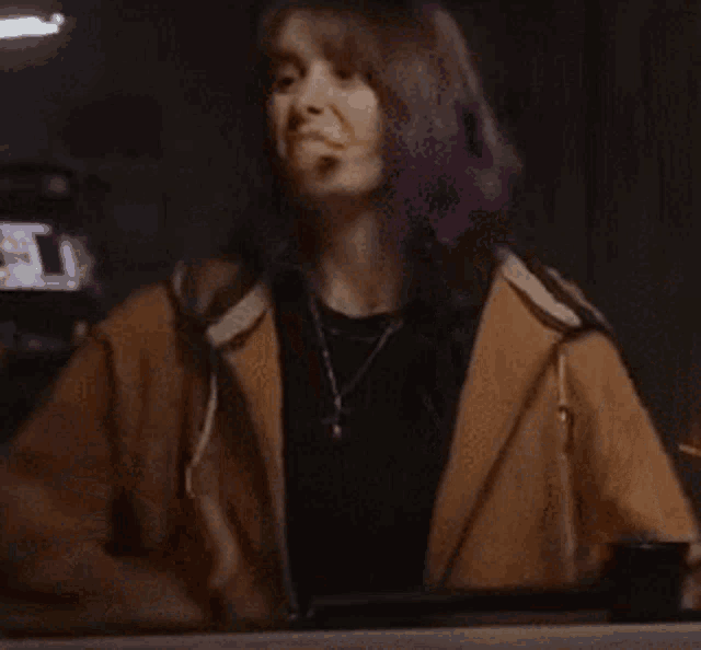 a woman with purple hair is sitting at a table wearing a hoodie and a necklace .