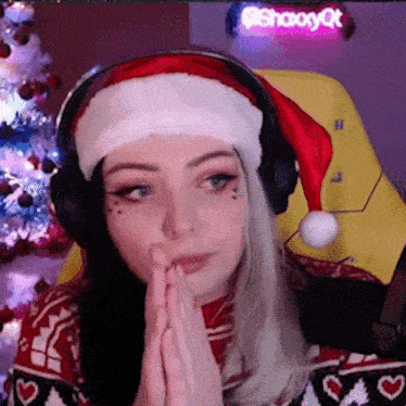 a woman wearing a santa hat and headphones is sitting in front of a christmas tree