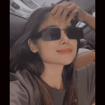 a woman wearing sunglasses is taking a selfie in the back seat of a car .