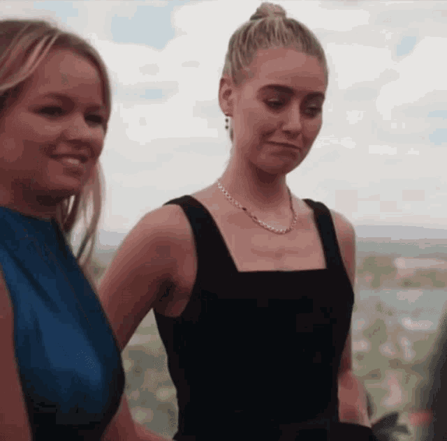 two women standing next to each other with one wearing a black dress