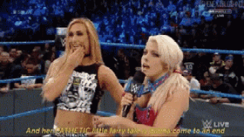 two women are talking into microphones in a wrestling ring while a crowd watches .