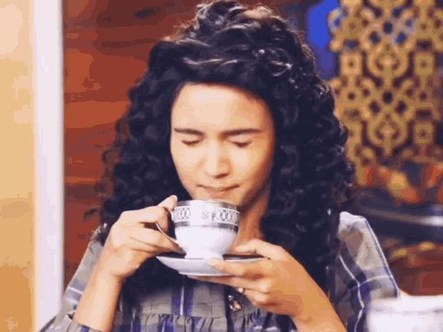 a woman with curly hair is drinking from a white cup with a silver rim