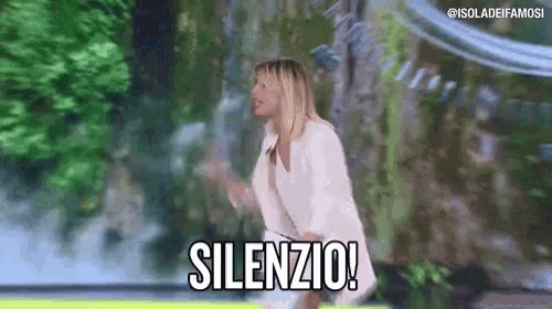 a woman in a white jacket is standing in front of a waterfall and shouting silence .