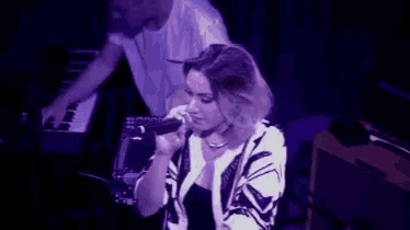 a woman is singing into a microphone on a stage while a man plays a keyboard in the background .