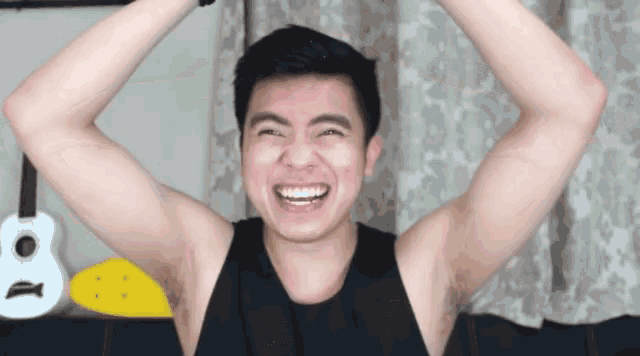 a man in a black tank top is smiling with his arms up in the air .