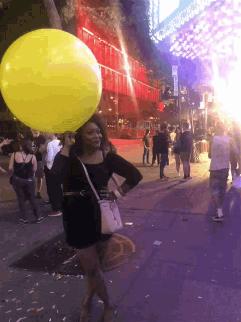 a woman with a yellow balloon on her head stands on a street