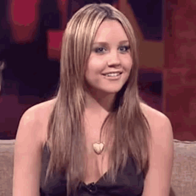 a woman in a black dress is sitting on a couch smiling .