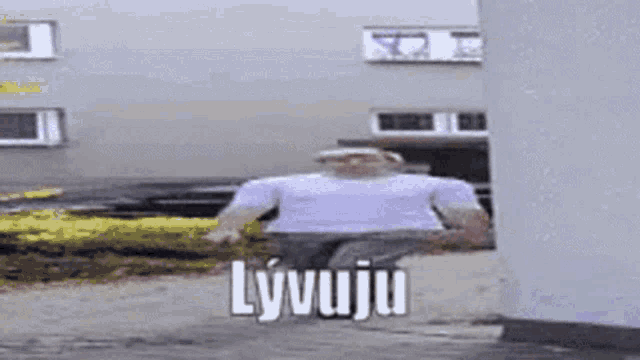 a man in a white shirt is running in front of a building with the word lyvuju written on the ground .