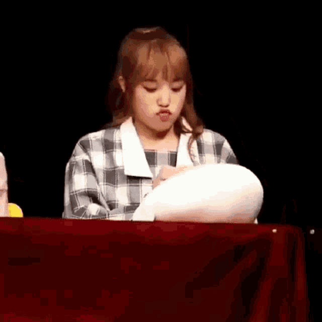 a girl is sitting at a table with a pillow in her hand .