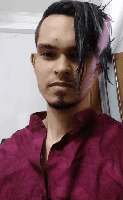 a man with a beard and a purple shirt has a reflection of another man 's face in his hair
