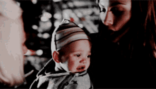 a woman is holding a baby in her arms and the baby is wearing a striped hat