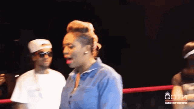 a woman in a blue shirt is standing in a boxing ring with a man in a white shirt behind her