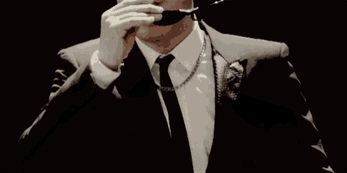 a man in a suit and tie is wearing sunglasses and a necklace .