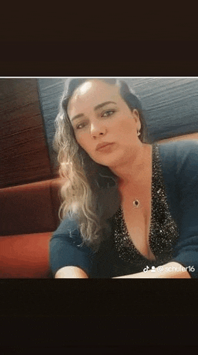 a woman is sitting on a couch wearing a plunging neckline sweater and earrings .