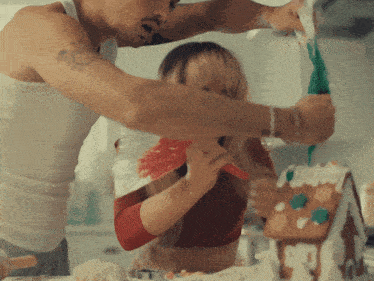 a man and woman decorate a gingerbread house