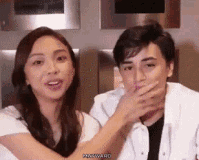 a man and a woman are sitting next to each other and the man is covering his mouth .