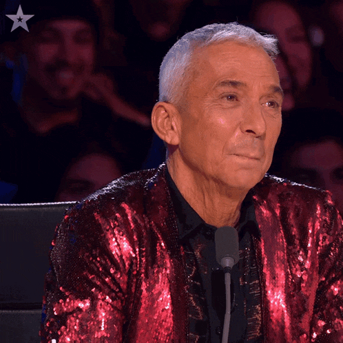 a man wearing a red sequined jacket sits at a microphone